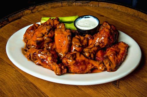 A plate of saucy chicken wings with celery sticks and a small cup of ranch dressing on a wooden table.