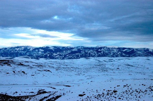 A vast snowy landscape under a cloudy sky, with distant mountains and rolling hills in the background.