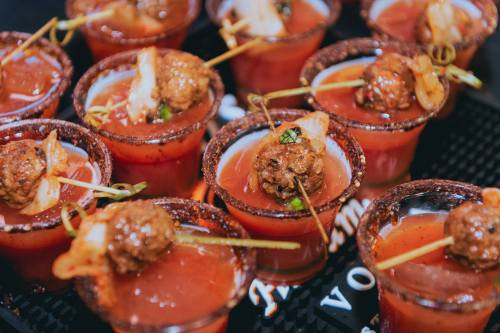 A close-up of small glasses filled with a red drink, each topped with a meatball and garnished with herbs.