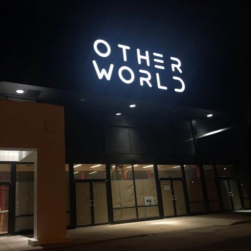 A dark storefront with a large illuminated sign reading "OTHER WORLD." Windows are covered, creating a mysterious atmosphere.