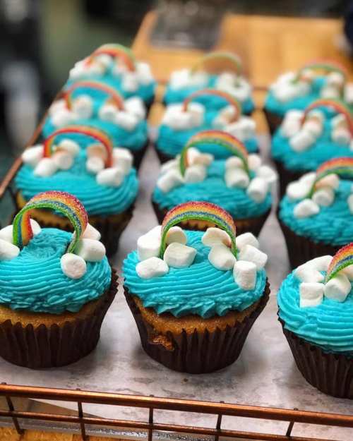 Colorful cupcakes with blue frosting, topped with rainbow candy and marshmallows, arranged on a wire rack.
