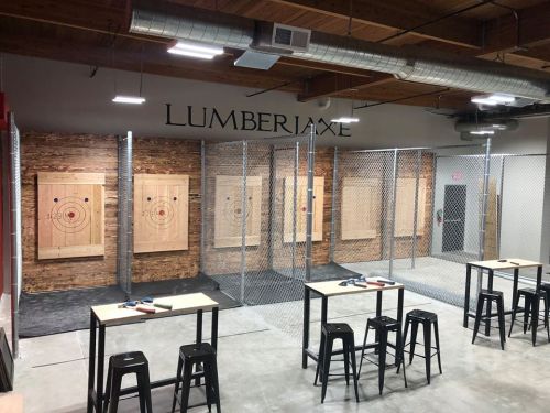 Interior of an axe-throwing venue with wooden targets, metal fencing, and tables for participants.