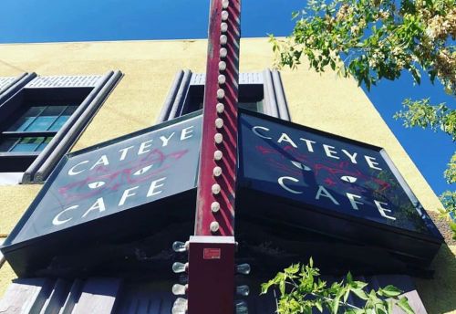 Sign for "Cateye Cafe" featuring a cat design, mounted on a building with a clear blue sky in the background.
