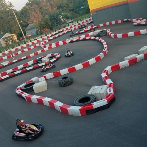 Aerial view of a go-kart track with red and white barriers, featuring several karts racing along the winding course.