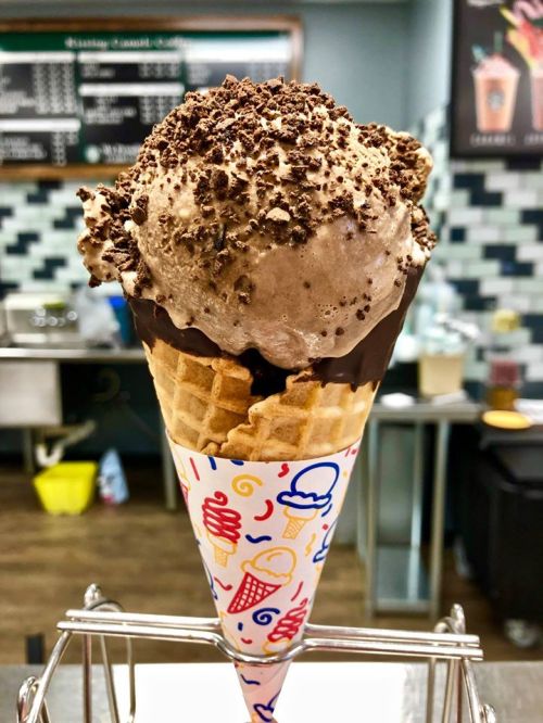 A delicious ice cream cone with chocolate ice cream topped with crushed chocolate pieces in a colorful cone.
