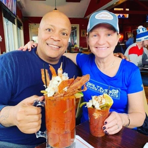 A man and woman smile together at a restaurant, each holding large cocktails with garnishes.