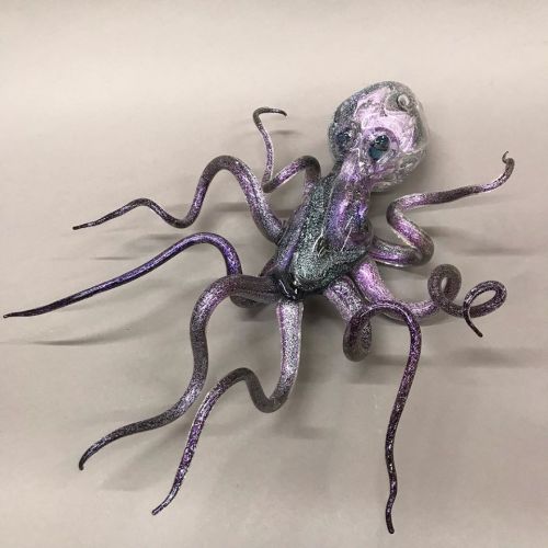 A glittery purple and silver octopus sculpture with long, curled tentacles on a neutral background.