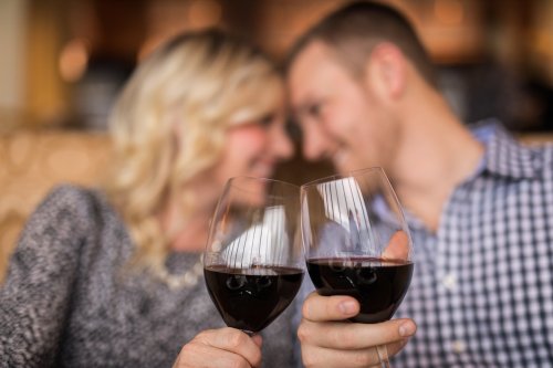 A couple toasting with glasses of red wine, smiling at each other in a cozy setting.