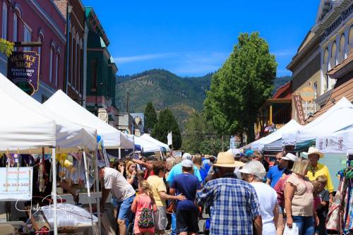 A bustling street market with people browsing tents, surrounded by mountains and clear blue skies.