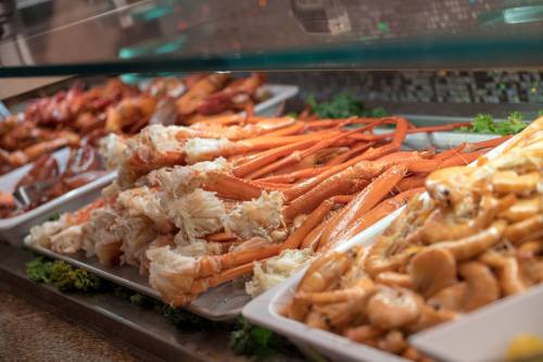 A seafood buffet featuring various dishes, including crab legs, shrimp, and lobster, displayed on white trays.