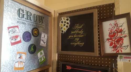 A display of framed art and stickers with inspirational quotes and gardening themes on a pegboard wall.