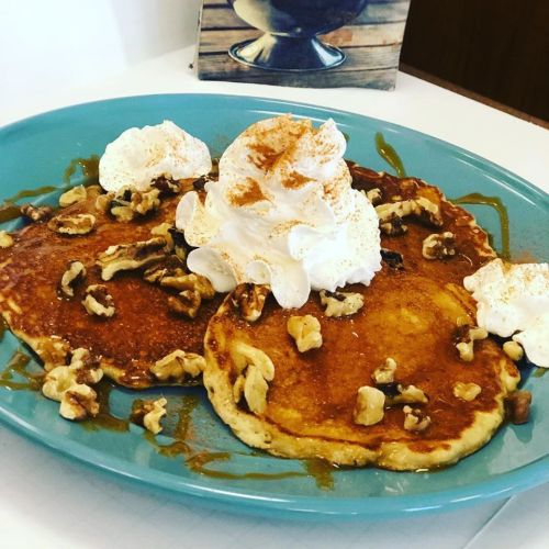 A plate of pancakes topped with whipped cream, walnuts, and a drizzle of syrup, served on a blue dish.