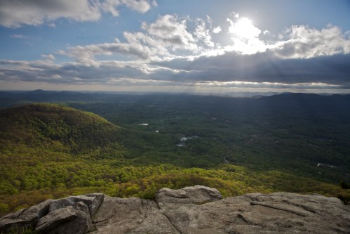 A panoramic view of lush green mountains under a cloudy sky, with sunlight breaking through the clouds.