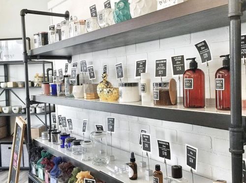 A display shelf with various candles, jars, and decorative items, each labeled with prices on small black signs.