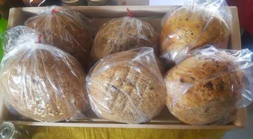 A wooden box filled with six loaves of bread, each wrapped in clear plastic bags.