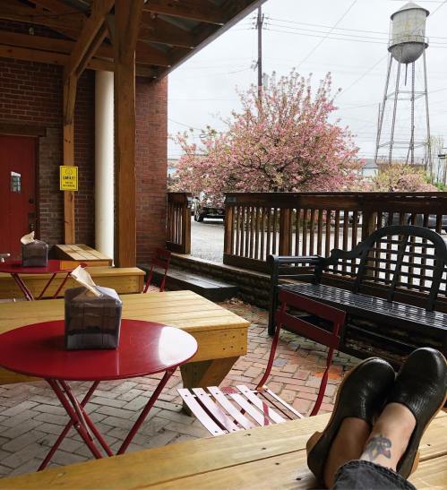 A cozy outdoor seating area with red tables, wooden benches, and blooming pink trees in the background.