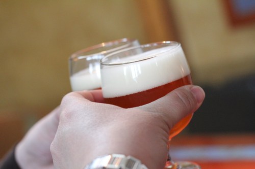 Two hands clinking glasses of beer, showcasing frothy tops and amber liquid.