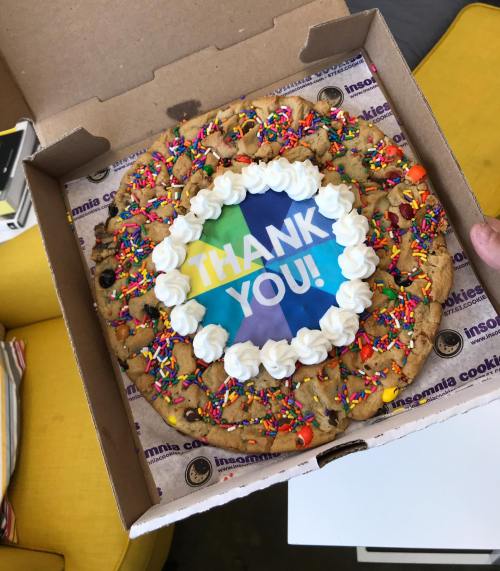 A large cookie cake in a box, decorated with colorful sprinkles, frosting, and a "THANK YOU!" message in the center.