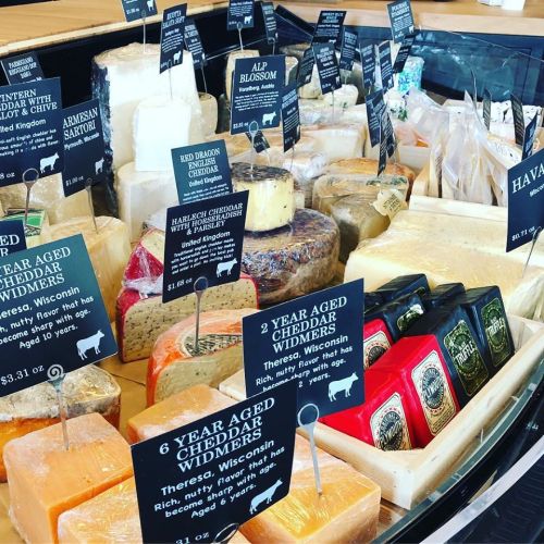 A display of various cheeses with labeled signs, showcasing different types and origins in a cheese shop.