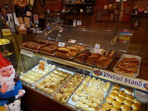 A display case filled with various baked goods, including pretzels and loaves of bread, in a cozy shop setting.