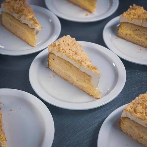 Slices of yellow cake with white frosting and crumb topping on white plates, arranged on a gray surface.