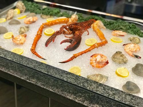 A seafood display featuring a large lobster, shrimp, clams, and lemon slices on a bed of ice.