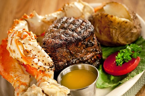 A plate featuring grilled steak, crab legs, a baked potato, and a small cup of melted butter.