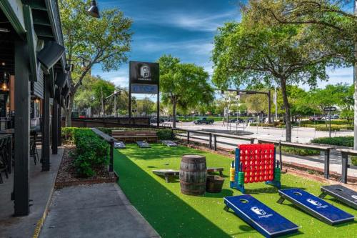 Outdoor area of a bar featuring cornhole games, a giant connect four, and green turf under a clear blue sky.