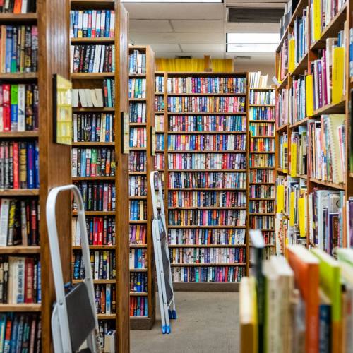A narrow aisle between tall bookshelves filled with colorful books in a cozy bookstore.