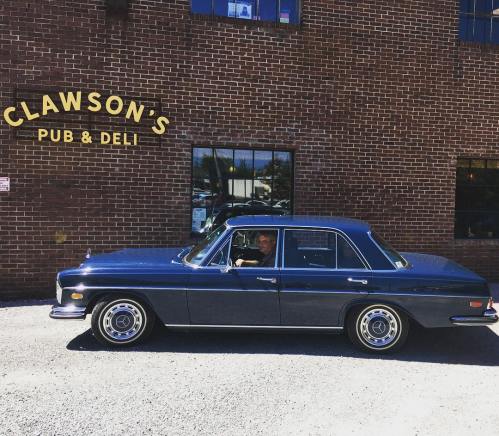 A classic blue car parked outside Clawson's Pub & Deli, with a person sitting in the driver's seat.