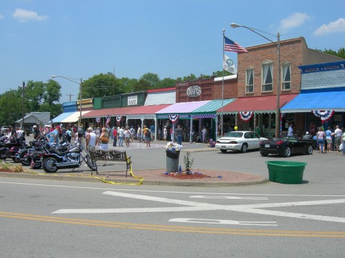 A bustling street scene with shops, people, and parked motorcycles, decorated for a festive occasion.