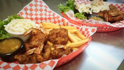 Two baskets of fried shrimp with fries, coleslaw, and dipping sauce, served on a checkered paper.
