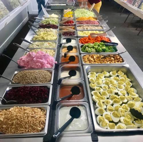 A buffet table filled with various salads, toppings, and sides, including deviled eggs, vegetables, and dressings.