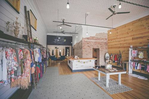 A stylish boutique interior featuring clothing racks, a reception desk, and a mix of brick and wooden walls.