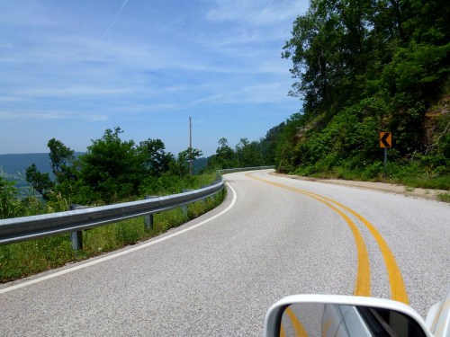 A winding road curves through lush greenery under a clear blue sky.