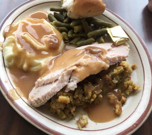 A plate of turkey with gravy, stuffing, mashed potatoes, green beans, and a roll.
