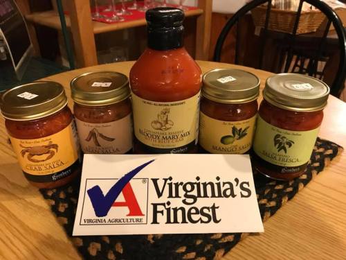Five jars of salsa and a bottle of Bloody Mary mix on a wooden table, with a "Virginia's Finest" sign in front.