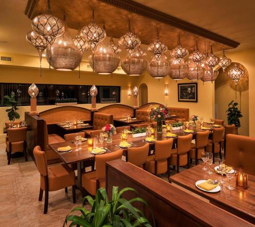 Elegant restaurant interior with warm lighting, wooden tables, and plush seating, adorned with decorative hanging lamps.