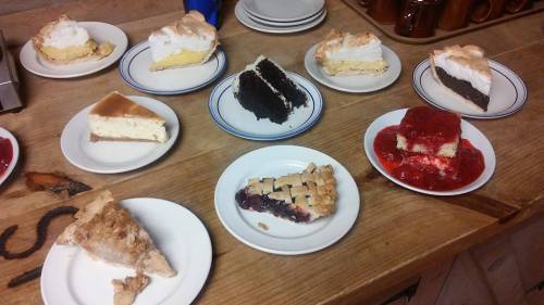 A variety of desserts on plates, including pies, cakes, and cheesecake, displayed on a wooden table.