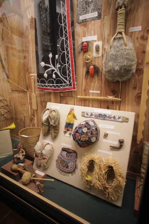 Display of traditional artifacts, including clothing, footwear, and decorative items, in a museum setting.