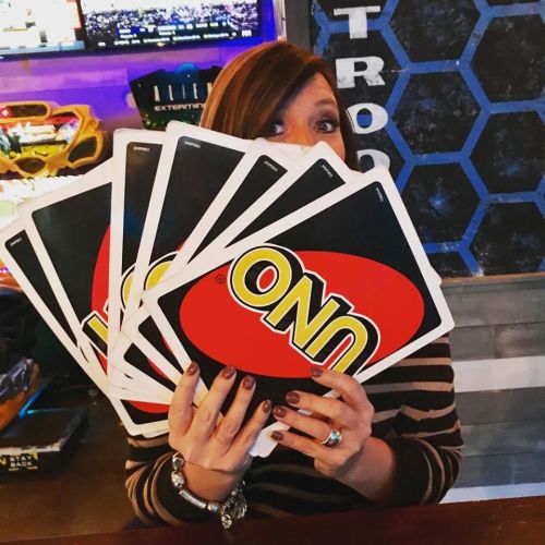 A person holds multiple UNO cards in front of their face, smiling, in a lively game setting.