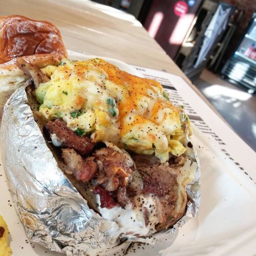 A loaded baked potato topped with scrambled eggs, cheese, and chunks of meat, served on a white plate.