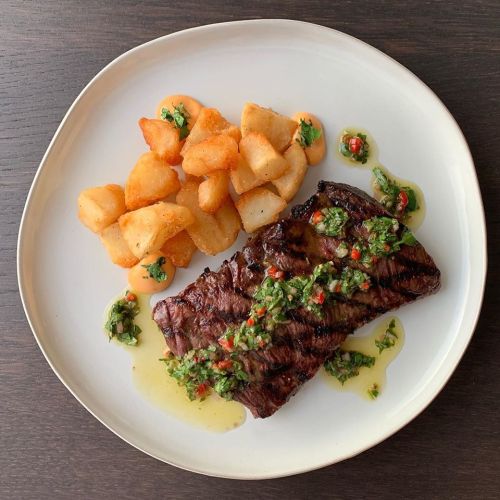 A plate featuring grilled steak topped with chimichurri sauce, accompanied by crispy potato wedges.