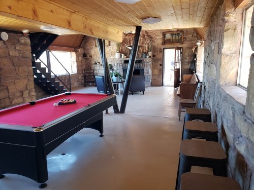 A cozy interior featuring a pool table, stone walls, wooden beams, and a seating area with a fireplace.