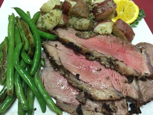 A plate of sliced roast beef, green beans, roasted red potatoes, and a slice of orange.