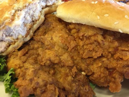 Close-up of a crispy fried chicken sandwich with lettuce and a sesame seed bun, served on a plate.