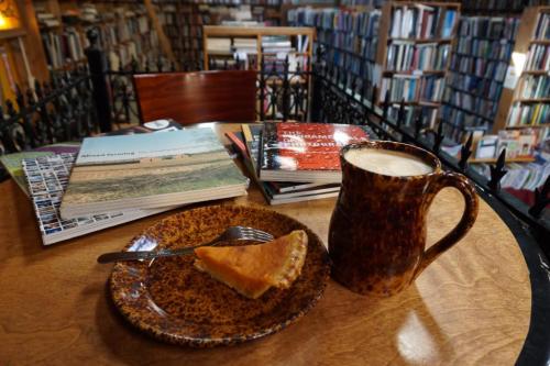 A cozy table with a slice of pie, a fork, a mug of coffee, and books stacked in a library setting.