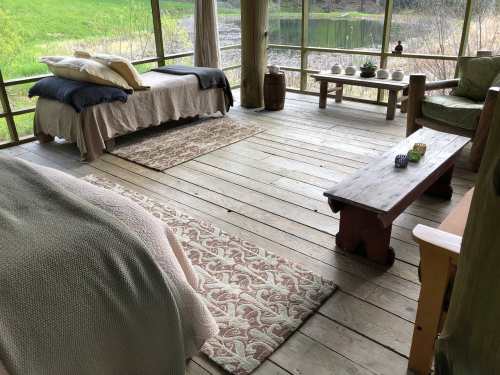 Cozy cabin interior with a bed, seating area, and wooden furniture, surrounded by nature and a serene view.
