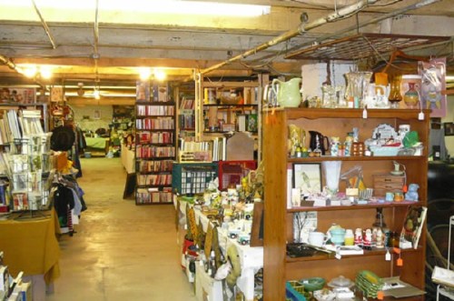A cozy thrift store aisle filled with shelves of various items, including books, antiques, and home decor.