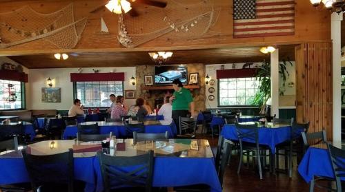 A cozy restaurant interior with blue tablecloths, diners chatting, and a server attending to guests.